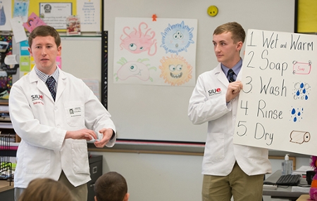 SIUE School of Pharmacy first-year students Andrew Moore (L) and Aaron Burge (R) give a presentation about hand washing to third grade students at Woodland Elementary in Edwardsville.