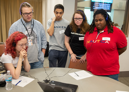 A group of students gather around a computer to view and listen to a digital narrative.