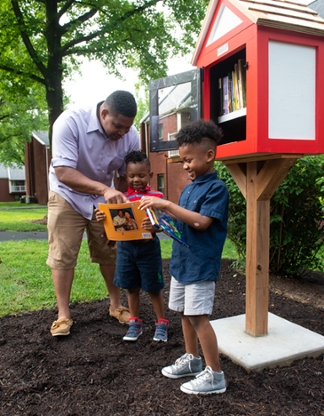 Cougar Village resident Tyrone Johnson and his sons, Charles and Tyrone, enjoy books from the new Little Free Library.