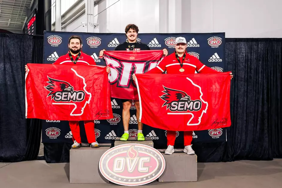 Male track and field athletes stand on an Ohio Valley Conference podium holding SIUE and SEMO flags, wearing medals during the OVC championship awards ceremony.