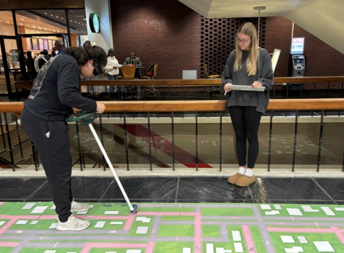 student uses goggles that simulate vision of someone under the influence to navigate on a map. EOA volunteer watches and takes notes