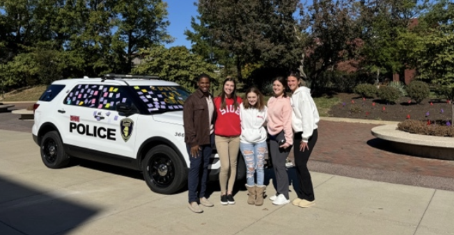 5 students in front of SIUE PD cruiser covered with post its