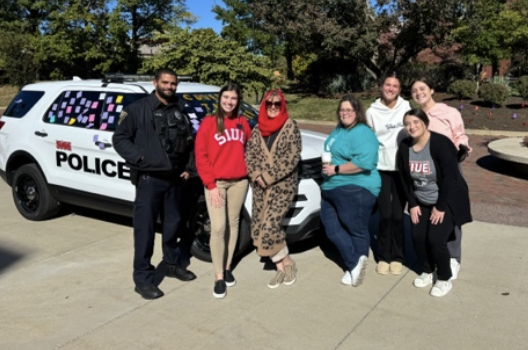 SIUE PD officer and 6 students standing in front of the cruiser