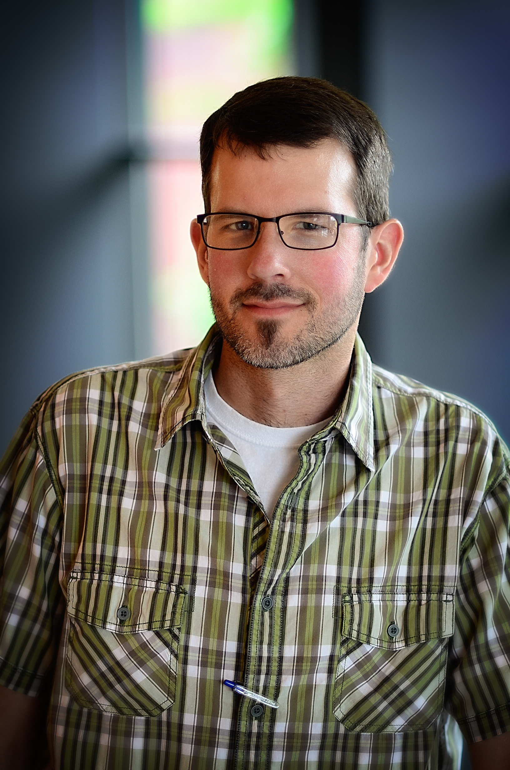 Man in glasses smiling in a plaid shirt. He has a beard.