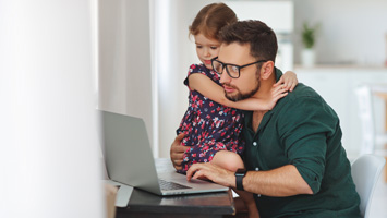man working on lap top with daughter on lap