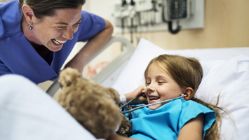 nurse laughing with child in hospital bed