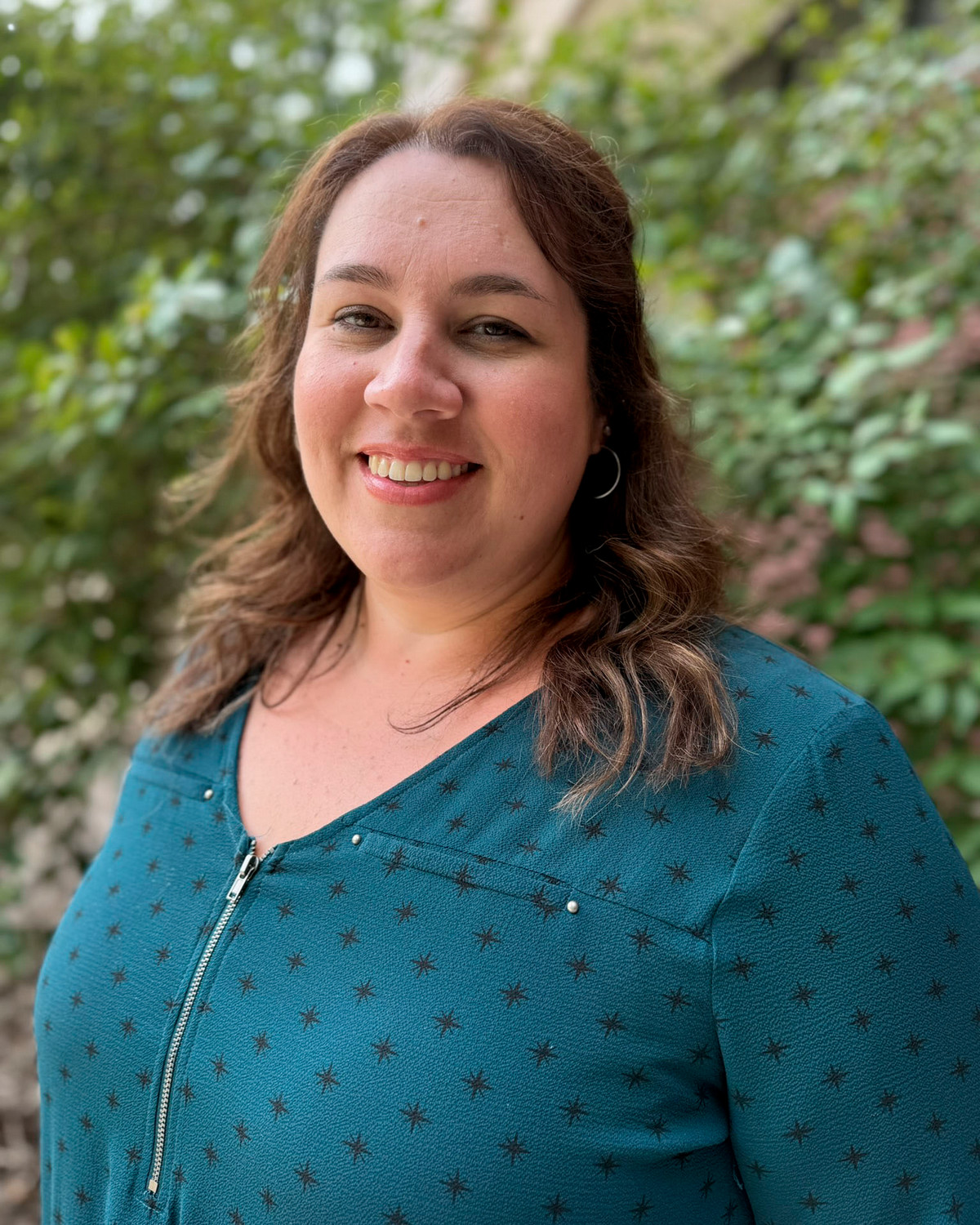 woman with brown hair and teal shirt in front of foliage