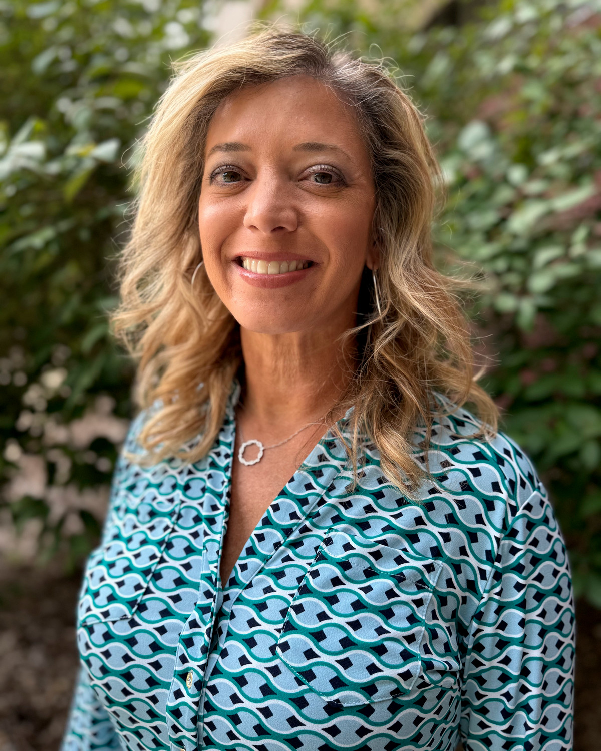 woman with blonde hair in print dress in front of foliage