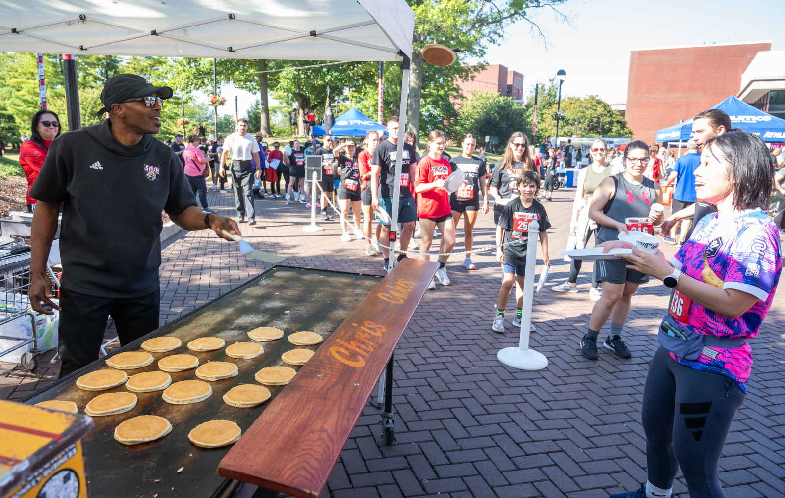 SIUE Chancellor James T. Minor flips pancakes on an outdoor griddle as runners line up for breakfast after the 2025 Cougars Unleashed Homecoming Run.