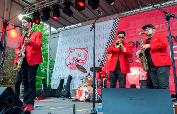 Band members in red jackets perform on an outdoor stage during the One Day One SIUE celebration.