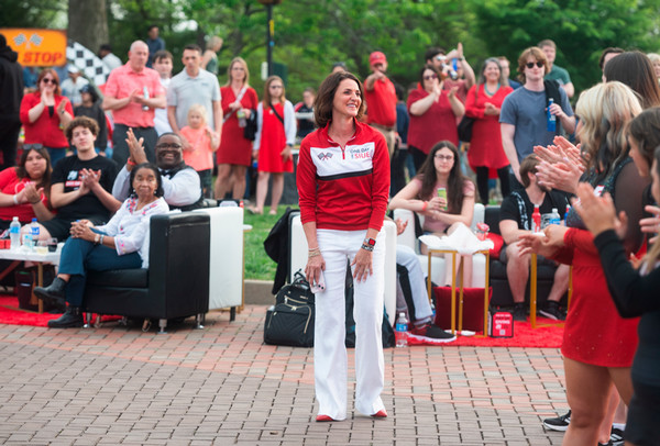 Woman in SIUE attire stands smiling as a crowd applauds around her during the One Day One SIUE celebration.