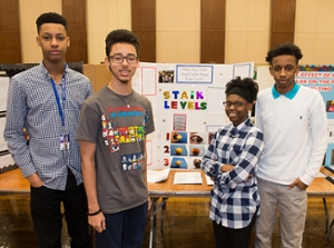 four students stand in front of their science project