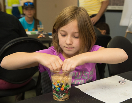 A camper engages in a hands-on activity that taught them about the layering processes at landfills.