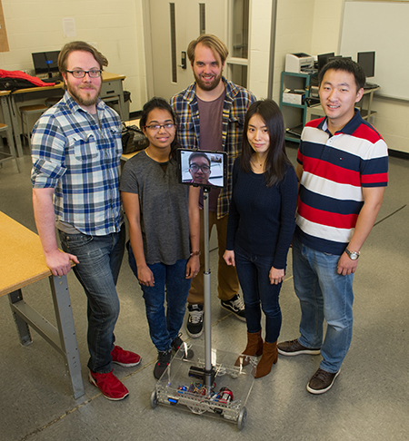 The SIUE School of Engineering research team working on the telepresence robot includes (L-R) Alex Dinan, Sherin John, Bryan Kier, Kai Li and Pengji Duan. Dr. Mingshao Zhang is seen on the robot's screen via remote access.