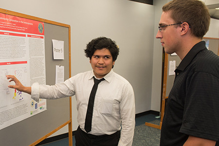 Alexander Huaylinos, a rising senior from the City College of New York, describes his research to a guest at the REU Symposium.