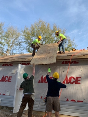 SIUE Constructor’s Club member Jakob Kunkel and a Habitat core volunteer hand a sheet of plywood to SIUE’s Adam Sullivan and Austin Mattingly.