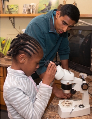 SIUE STEM Center Graduate Assistant Manuel Gomez looks on as a student uses a microscope during the after-school Urban Gardening program.