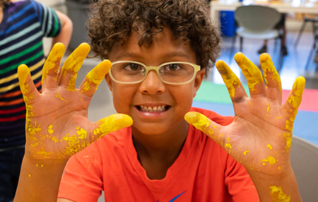 An SIUE Summer Arts Camp participant smiles while working on a messy, but fun art project.