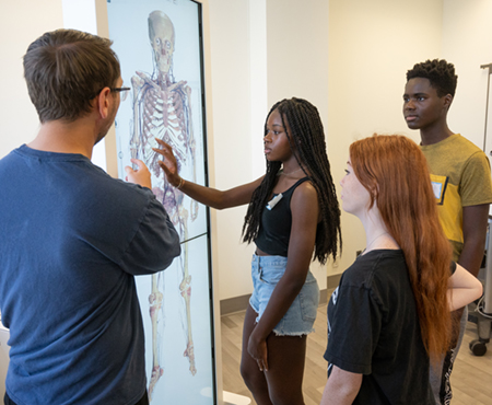 SIUE Teaching Assistant Nick Bauder (far left) shows the School of Nursing’s Anatomage Table to campers, including (L-R) Eva Cregler, of Oak Park, Alyssa Muir, of Gillespie, and Chibuike Azogini, of Collierville, Tenn.
