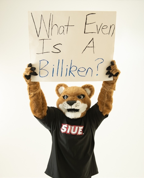 Eddie holding a sign above his head that reads "What Even Is A Billiken?"