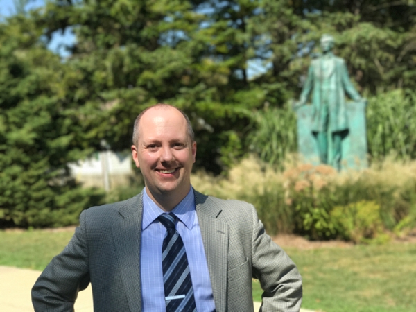 Professor Erik B Alexander standing in front of leafy trees