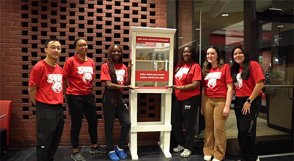 SIUE students surround a mini Cougar Cupboard food pantry