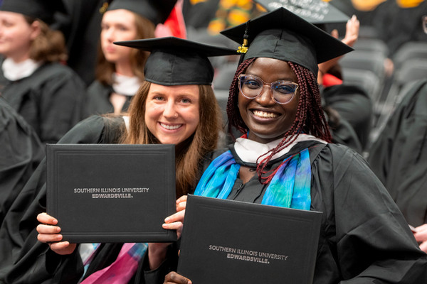 Two Graduates pose with diplomas at graduation