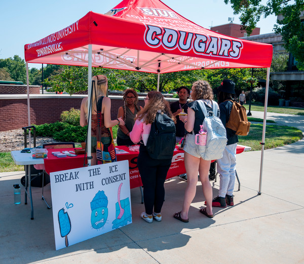 Photo of the break the ice with consent event featuring a pop up tent from SIUE and practicum students distributing resources and engaging with students about consent on a sunny day in the quad.
