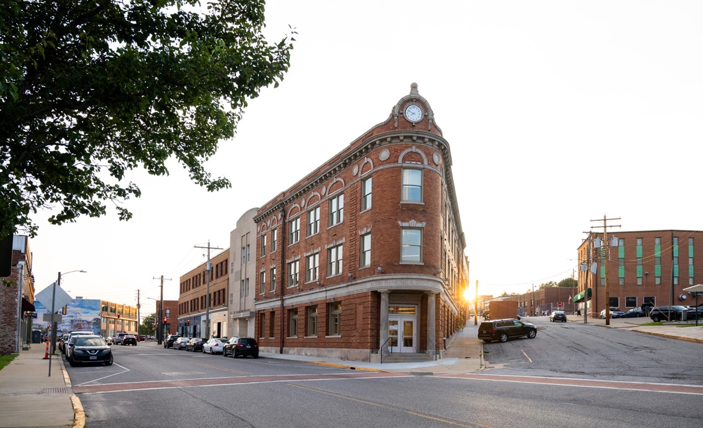 Photo of the Wedge building in Alton at sunset. It is a historic triangle shaped building with art nouveau elements, a clock, and brick stone masonry. This view bisects a corner, revealing two streets.