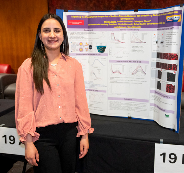 Student stands and poses for camera in front of research poster presentation