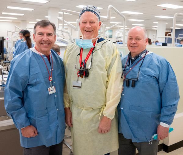 Three dentists dressed in clinic protective wear pose for camera