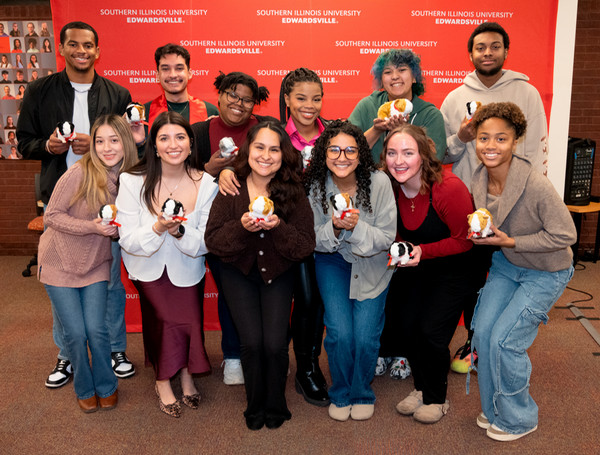 Seniors hold guinea pig stuffies and pose in front of SIUE background