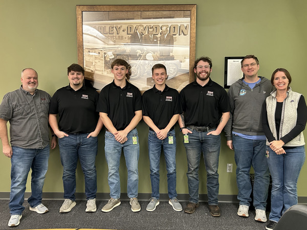 Team of people standing in front of wall with Harley Davidson image behind them