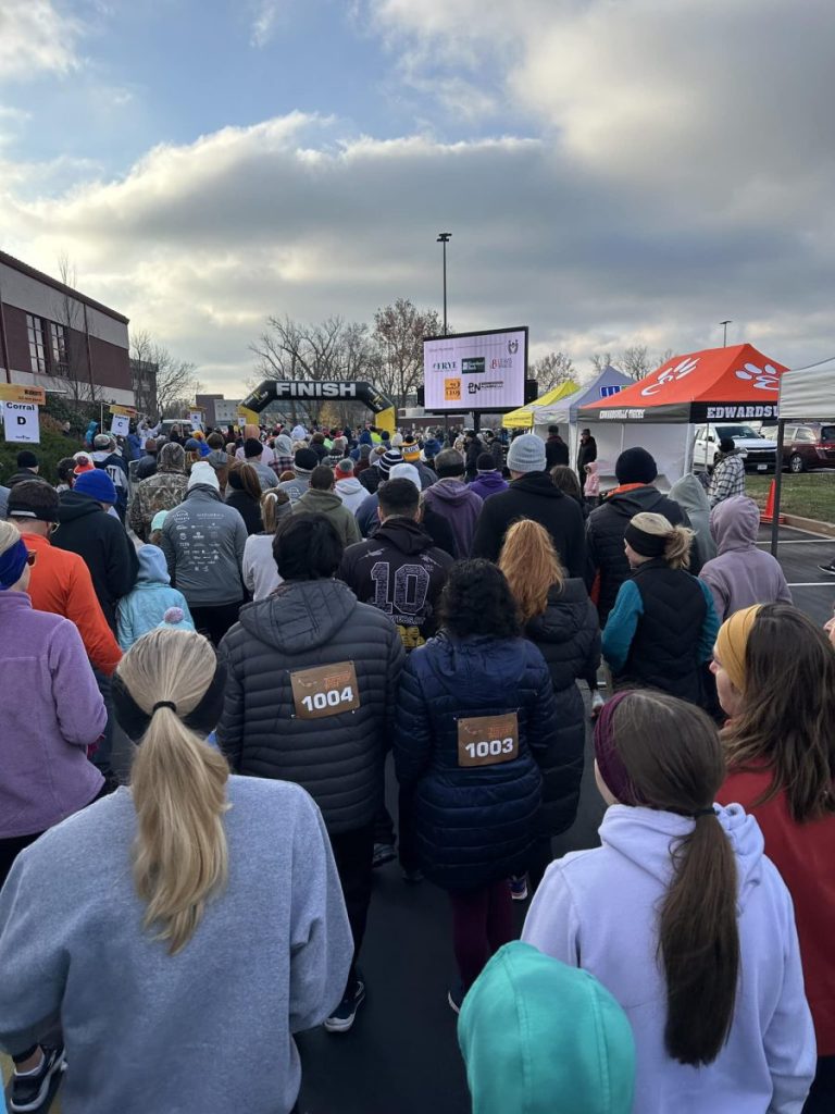 A large group of participants gathers near a finish line at an outdoor community run on a cold morning.