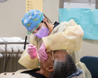 A healthcare provider wearing protective gear performs a dental procedure on a patient in a clinical setting.