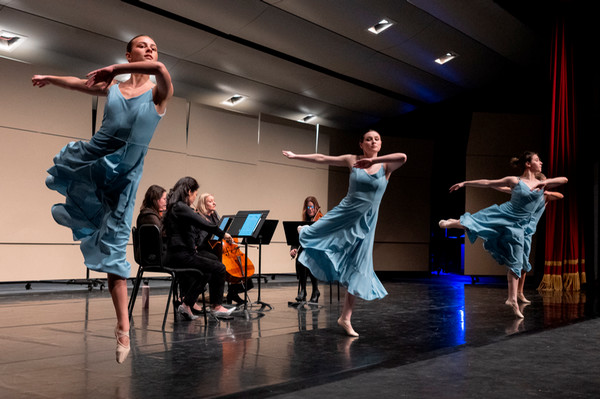 Dancers in blue costume dresses on stage with orchestra