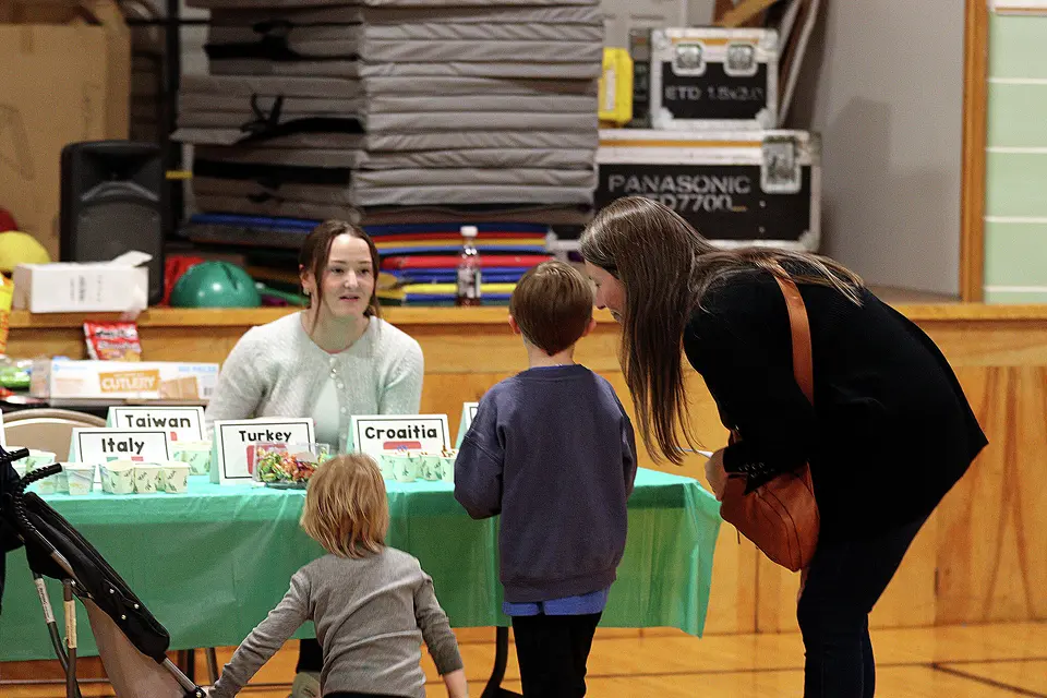 Children and an adult interact at a table displaying information about different countries inside an activity space at LeClaire Elementary.