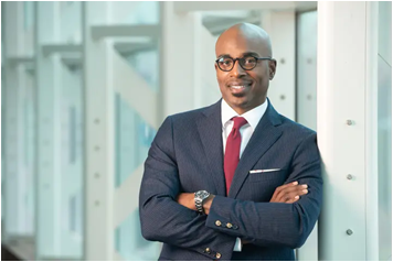 Chancellor James T. Minor stands with arms crossed in a professional portrait, wearing a suit and tie inside a campus building.