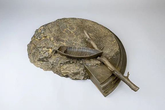 A bronze sculpture by Duhigg featuring layered, textured, stone-like forms with embedded organic elements, displayed against a light background.