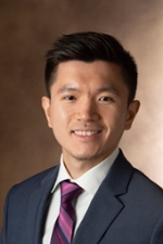 Jie Ying poses for a professional headshot wearing a suit and tie against a neutral background.