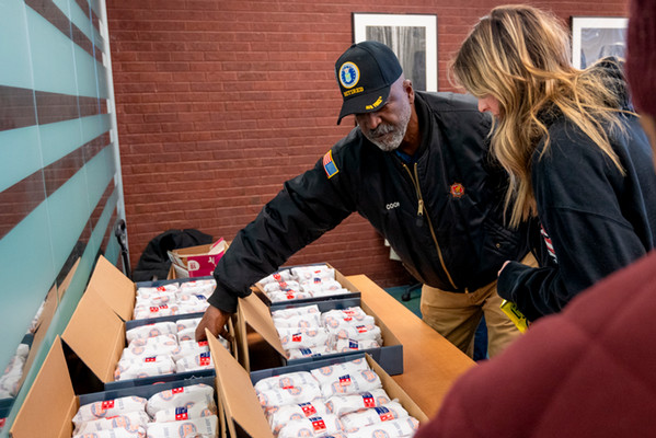 Retired Air Force veteran selects a boxed meal from a table filled with packaged lunches as a staff member assists.