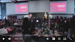 Wide view of a large banquet hall filled with attendees seated at round tables during an MLK celebration event, with presentation screens and flags visible at the front of the room.