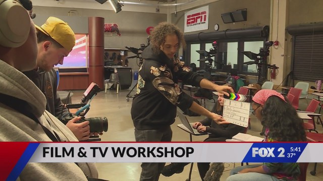 Students participate in a film and TV production workshop, with one person holding a clapperboard while others operate cameras in a studio classroom setting.