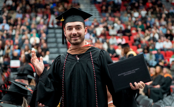SIUE graduate Dawson stands in academic regalia holding his diploma cover during commencement ceremonies at the Vadalabene Center.