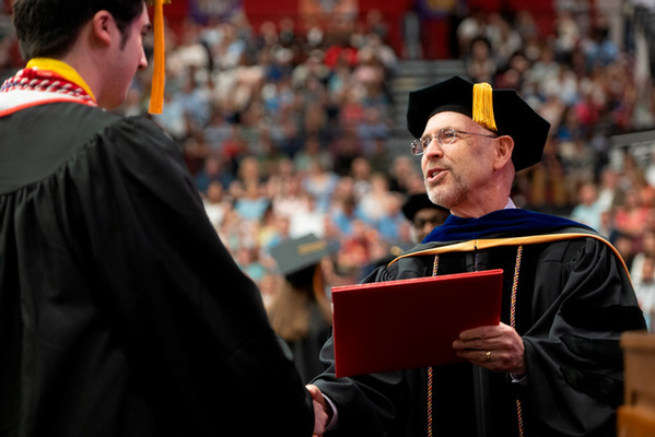 Dean Kevin Leonard in the College of Arts and Sciences awards an honor student with his diploma. The student and dean are dressed in formal academic regalia.