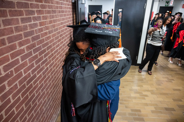 Air Force officer hugs his twin sisters during student commencement procession with onlookers