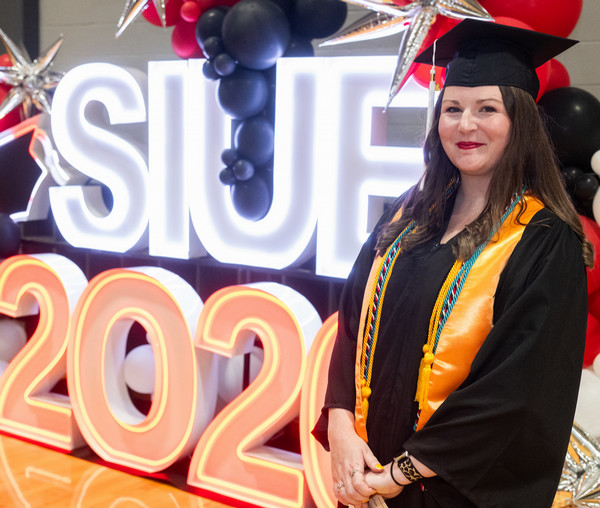 Student Thole in her cap and gown standing near glowing SIUE 2026 signage