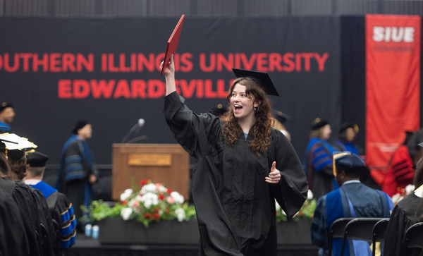 Woman with diploma up in the air walks from commencement stage to audience