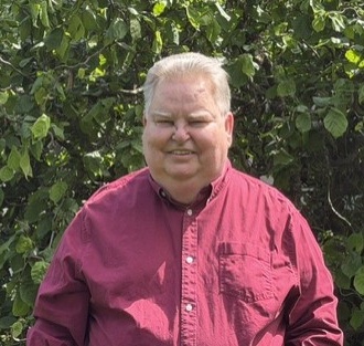Portrait of Drew Dolan standing in front of large leafy bush
