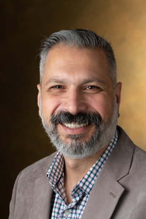 Portrait of Sinan Onal, PhD, chair of the Department of Industrial Engineering at Southern Illinois University Edwardsville, smiling while wearing a tan blazer and patterned button-down shirt against a neutral studio background.